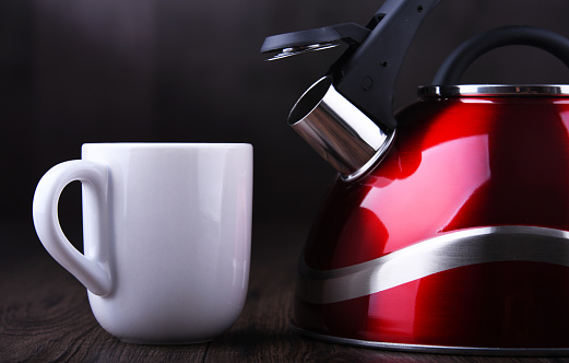 Red stainless steel stovetop kettle with whistle and cup of coffee