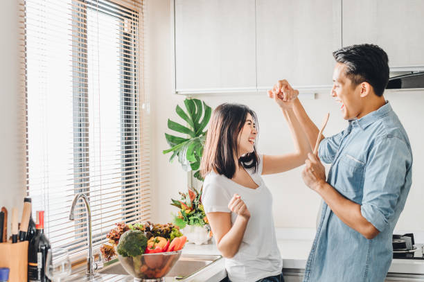 le couple dans l'amour danse et sourit tout en cuisinant ensemble dans la cuisine - asian cuisine photos photos et images de collection
