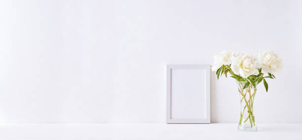istock Home interior with decor elements. Mockup with a white frame and white peonies in a vase on a white background 1199465814
