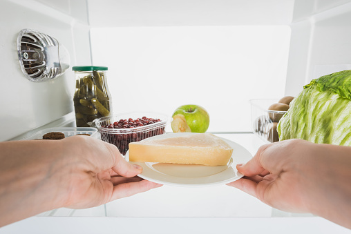 Cropped view of woman taking cheese from fridge with fruits and pickles isolated on white