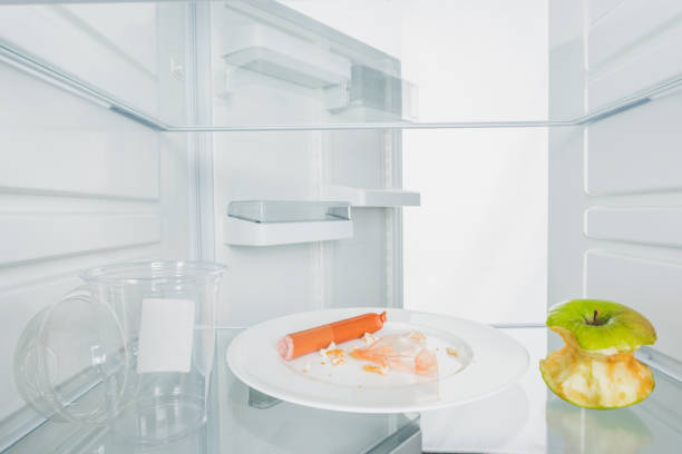 istock Plate with scraps, bitten apple and plastic cup in fridge with open door isolated on white 1199466786