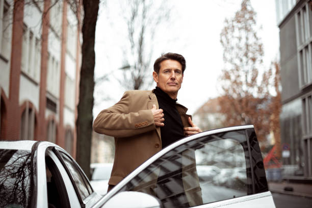 On the right place Handsome 55-year-old man just arrived to his destination by car and how taking coat on. georgijevic frankfurt stock pictures, royalty-free photos & images
