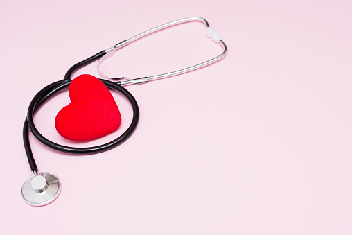 black medical stethoscope with red heart on on pink background. medicine love concept. Flat lay, top view