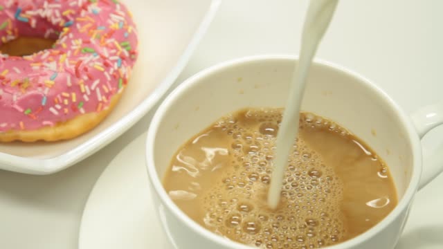 Pouring milk in a coffee cup and strawberry donut