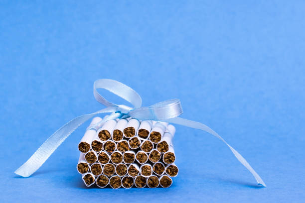 istock A stack of new thin cigarettes is tied with a blue ribbon with a bow lying on a blue background. The danger of smoking for women. Fatal addiction. 1199493060