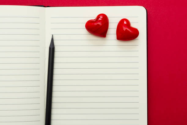 istock Valentine's Day. Open notebook with red hearts and a pencil, on red background, copy space for text. 1199505682