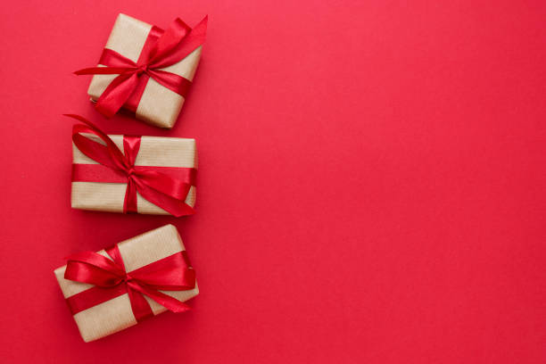 istock Gift boxes wrapped with kraft paper and red bow isolated on red background. Abstract flat lay. 1199506579