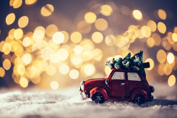 Toy car with Christmas tree driving in snow. Christmas lights background.