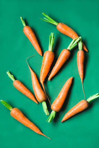 istock several fresh carrots lie in a row on a green background. 1199509225