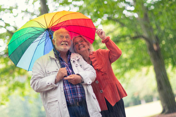 senior couple out in rainfall - umbrella senior adult couple autumn imagens e fotografias de stock