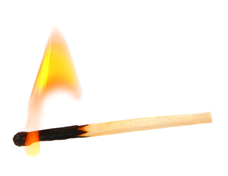 Close-up of igniting matchstick against coloured background.