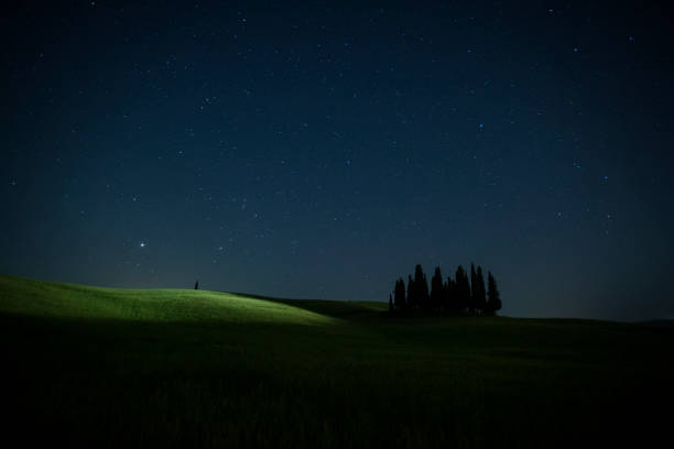 Hills in Tuscany (Italy) at night with a cypress forest in silhouette panorama of the Tuscan hills in spring at night, with the starry sky and on the horizon in silhouette a cypress forest in the Val d'Orcia. crete senesi stock pictures, royalty-free photos & images
