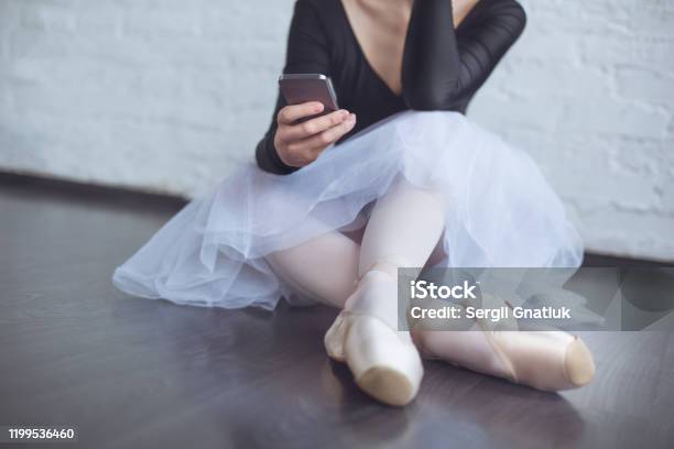 Young Ballet Dancer Sitting Leaning White Wall Using Phone In Studio Active Lifestyle Closeup Stock Photo - Download Image Now
