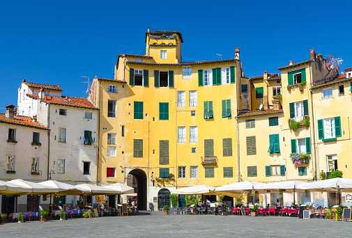 Piazza dell Anfiteatro square in circus yard of medieval town Lucca historical centre, old colorful buildings with shutter windows and blue clear sky background, Tuscany, Italy