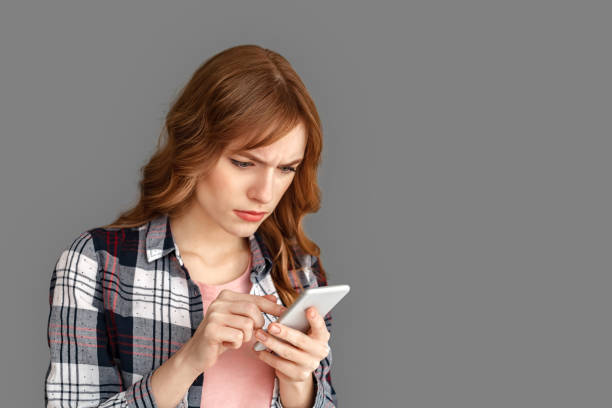 istock Copy Space for Text or Product . Stylish woman studio standing isolated on grey using app on smartphone touching sreen concerned close-up 1199536965