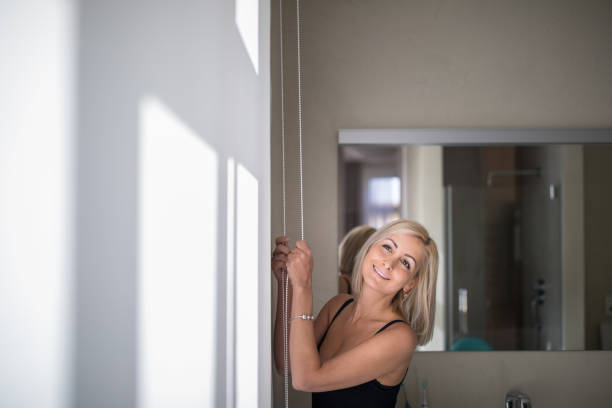 Pretty, young woman lowering the interior shades/blinds Pretty, young woman lowering the interior shades/blinds in her modern interior apartment honeycomb pattern photos stock pictures, royalty-free photos & images