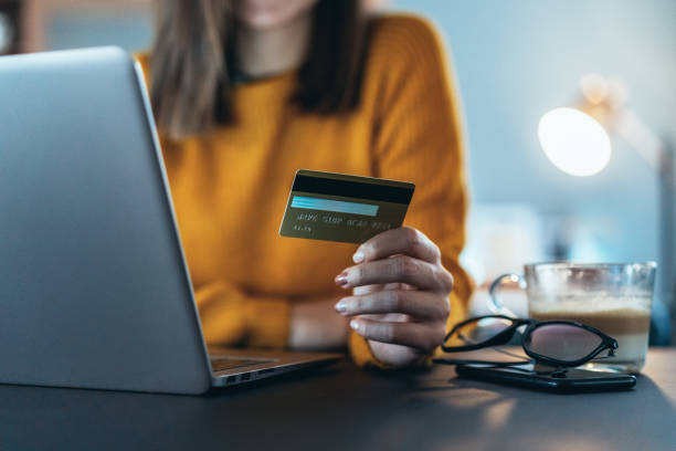 Online payment Unrecognizable person's hand holding credit card in front of lap top at home money transfer photos stock pictures, royalty-free photos & images
