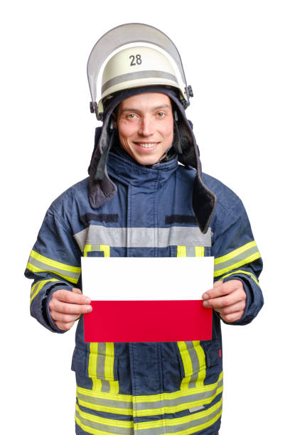 junger lächelnder feuerwehrmann schaut in die kamera und hält papierblatt mit polnischer flagge - löschpapier stock-fotos und bilder