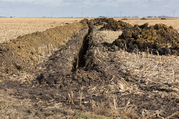 trincheira escavada no campo da exploração agrícola com pilhas do solo. tubulação da drenagem de água, telha do campo, instalação - controla da erosão - fotografias e filmes do acervo