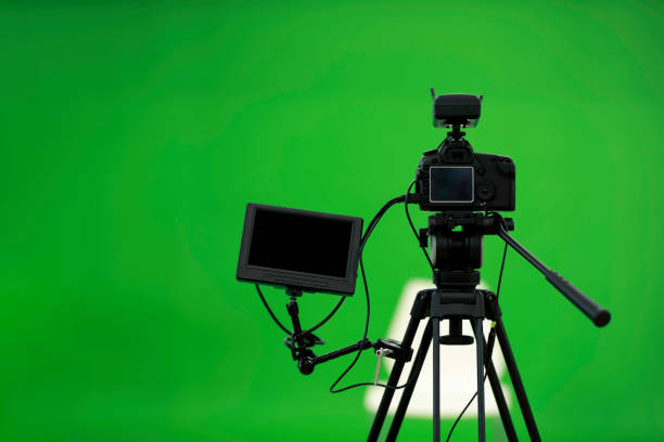 istock Camera on tripod connected with monitor on green screen background. 1199555096