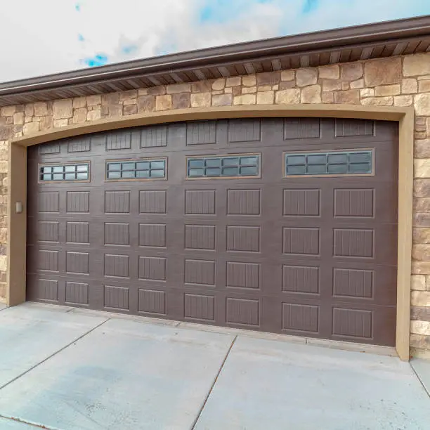 Square frame Large closed double wooden garage door in an ornamental face brick home with paved forecourt