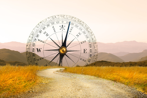 A large compass at the beginning of a dirt trail that leads toward a series of mountain ranges in the distance.