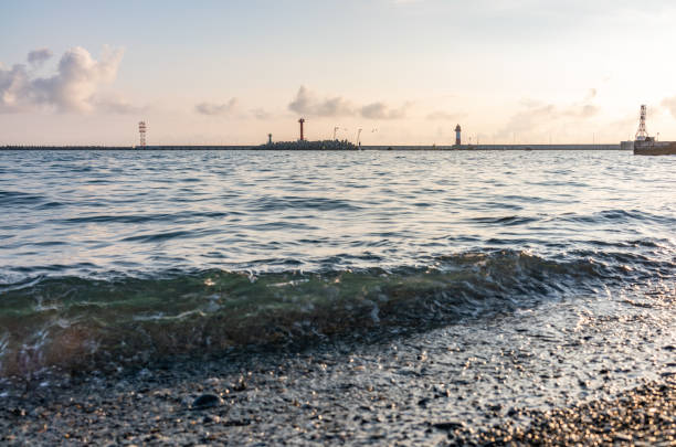 Sea harbor with breakwater and lighthouse at sunset. Sea wave at sunset.