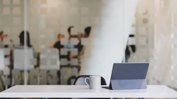 Close up view of comfortable workspace with digital tablet, coffee cup and copy space on white table with blurred office room background