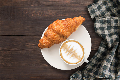 Coffee cup and fresh baked croissants near hand towel on wooden background. Top view, Copy space.