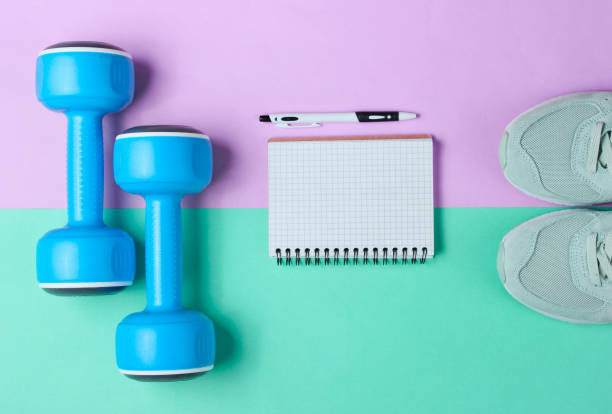 istock Fitness concept, workout plan. Plastic blue dumbbells, sport shoes, notepad on pastel background. Top view. Flat lay 1199570148