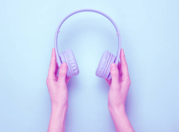 istock Women's hands holds wireless over-ear headphones on blue pastel background. Duotone effect. Minimalism. Top view 1199570203
