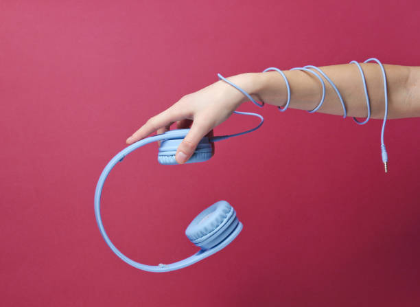 istock Hand wrapped cable holds blue headphones on red background 1199570765