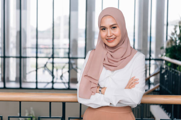Young happy and successful South East Asian Islamic business woman with arms crossed in business corporate building setting looks at camera stock photo