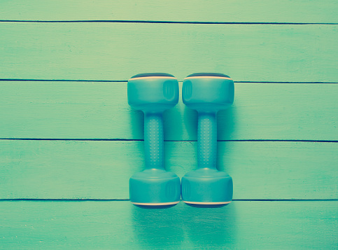 Two plastic blue dumbbells on blue wooden background. Top view.