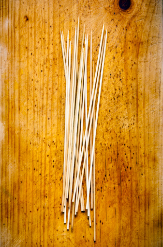 Wooden skewers sit in a rough pile on a timber board