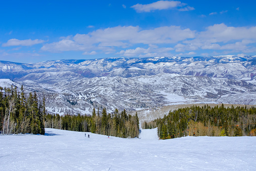View of Aspen-Snowmass Colorado ski resort landscape with spruce trees, mountains, and blue sky; nice winter day