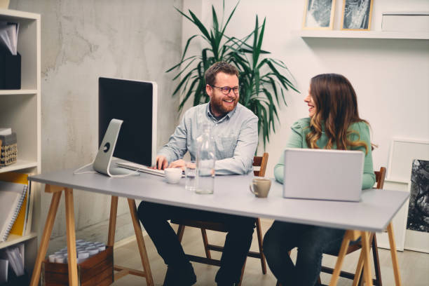 istock Two coworkers smiling and typing on computer in office. 1199596723