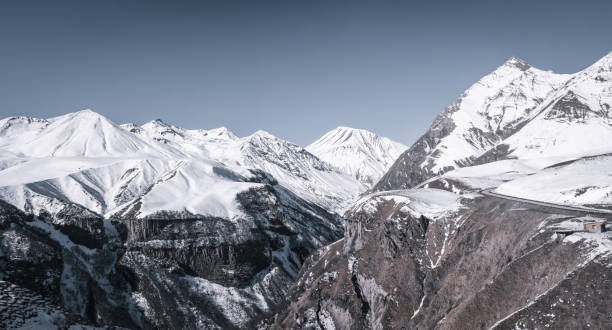 istock Snow-capped mountain range peaks. Blue sky on a clear winter day. Rocky cliffs in a mountain gorge. Panoramic view of the road through the pass. 1199597687