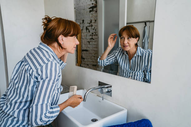 Senior woman adjusting hair in bathroom Senior Argentinian woman adjusting her hair in front of a mirror in bathroom. hair care women mature adult human skin stock pictures, royalty-free photos & images