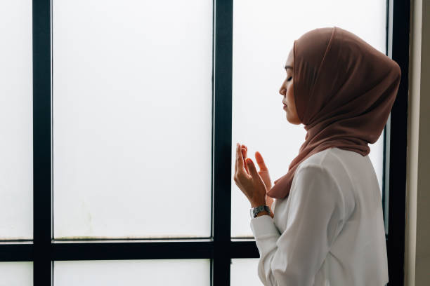 Islamic woman praying near window stock photo