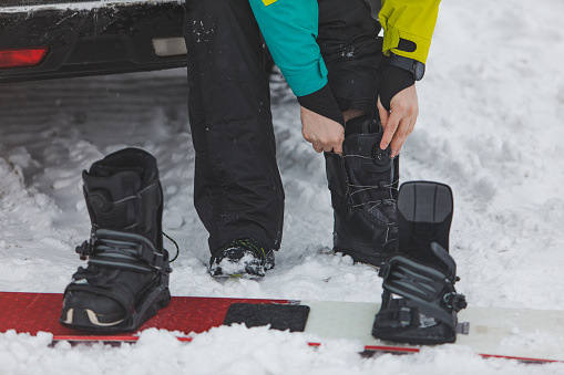 man changing regular boots to snowboard at parking place near car