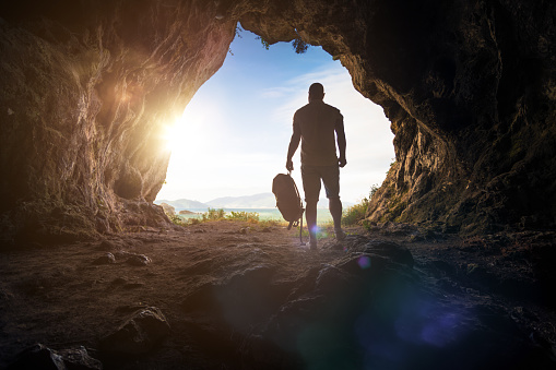 Traveler stands at the cave entrance at sunset