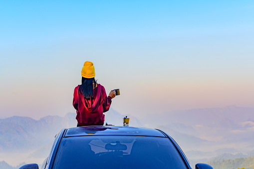 Woman traveller enjoy coffee time on her owns roof of the car with scenery view of the mountain and mist morning in background