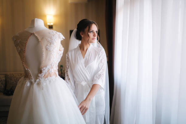 istock Young and beautiful bride stand by her wedding dress 1199606441