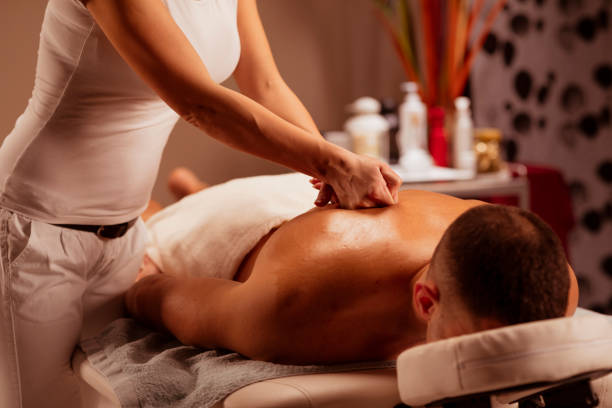 femme de thérapeute de massage faisant le massage curatif. homme appréciant dans le massage relaxant au traitement de spa de santé. - massage sensuel photos et images de collection