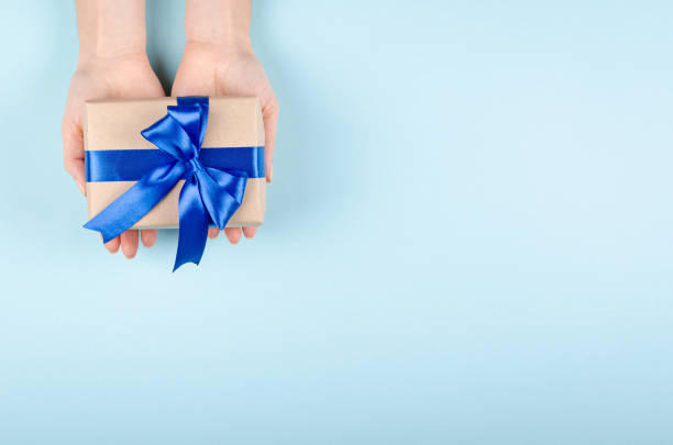 istock Hands with gift box on blue background composition, present with ribbon and bow. 1199610414