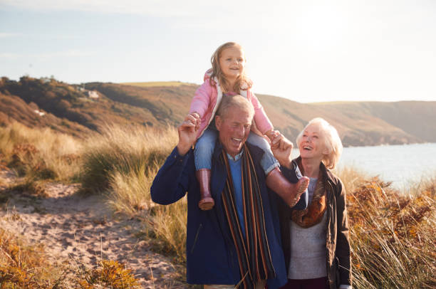 nonno che dà alla nipote un giro sulle spalle mentre camminano attraverso le dune di sabbia con la nonna - family happiness outdoors autumn foto e immagini stock