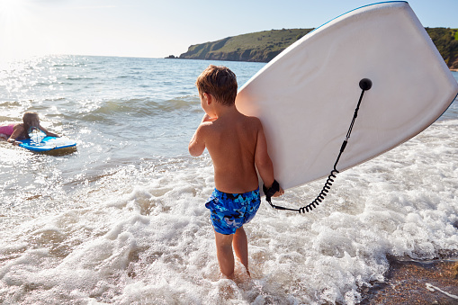 Children Playing In Sea With Bodyboards On Summer Beach Vacation