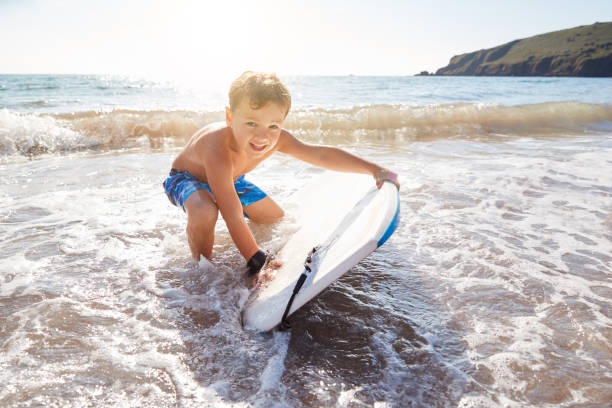 Boy Playing In Sea With Bodyboard On Summer Beach Vacation Boy Playing In Sea With Bodyboard On Summer Beach Vacation body board stock pictures, royalty-free photos & images