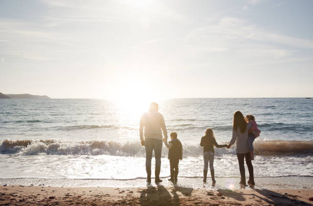 vista trasera de la familia mirando hacia el mar silueta contra el sol - familia con tres hijos fotografías e imágenes de stock